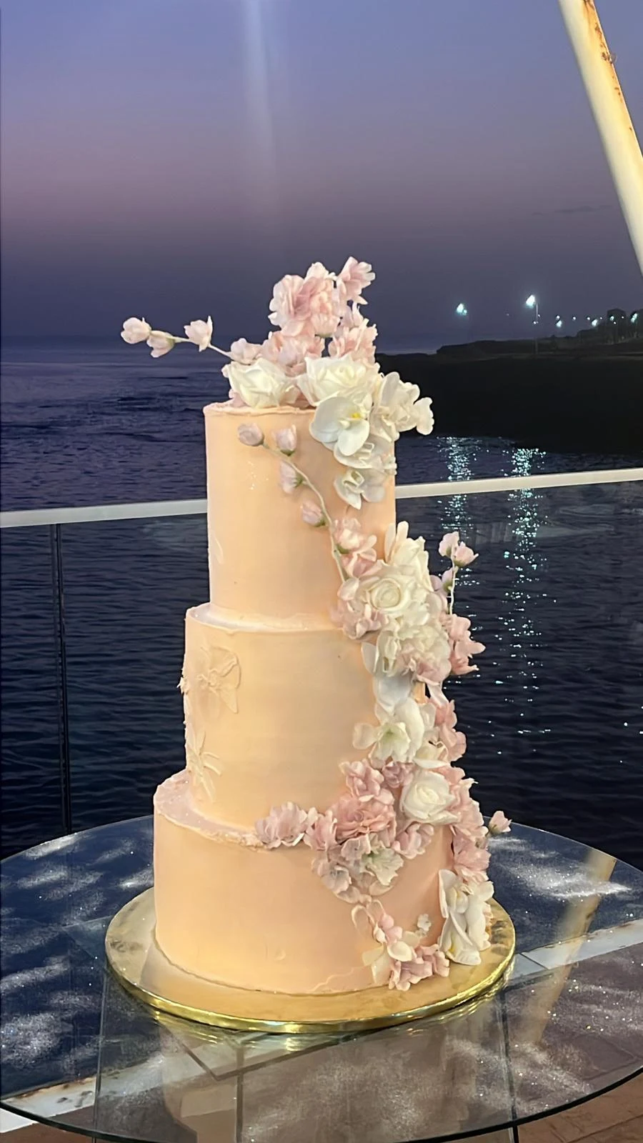 Bolo de batizado com três andares e flores rosadas.