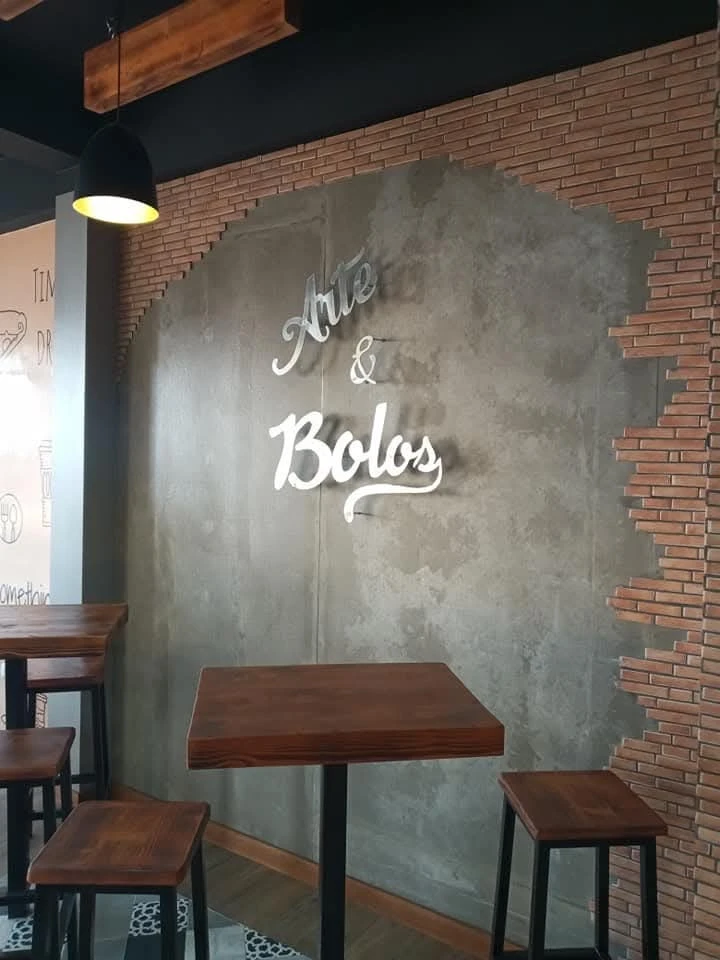 Interior da Arte & Bolos na Cidadela, com a marca na parede e mesas altas de madeira.